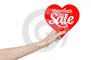 Valentine's Day and sale topic: Hand holding a card in the form of a red heart with the word Sale isolated on white background