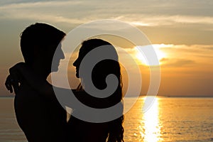 Valentine`s Day scene of a young couple silhouettes hugging at sunset by the ocean