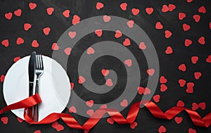 Valentine`s day table setting with plate, knife, fork, red ribbon and hearts on festive black background. a gift to your beloved