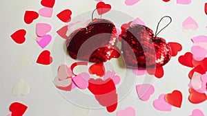 Valentine`s Day. Two red hearts made of sequins and confetti from multicolored hearts sway on a white background