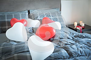 Valentine`s day and wedding anniversary. Heart shaped balloons above bed. Romantic scene with candles and gift box