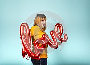 Valentine`s Day. Word love letters from inflatables. Funny girl holding a big word love with big smile on blue background