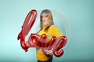 Valentine`s Day. Word love letters from inflatables. Girl holding a big word love on blue background