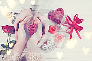 Valentine`s Day. Young couple hands holding gift box over white wooden background