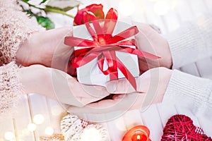 Valentine`s Day. Young couple hands holding gift box over white wooden background. Love concept