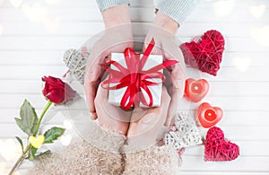Valentine`s Day. Young couple hands holding gift box over white wooden background