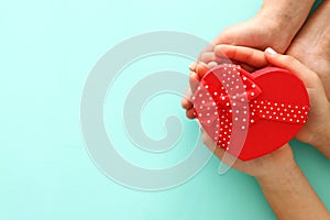 Valentine`s, father`s and mother`s day background. Little child with mother heands holding red heart present box. Top view