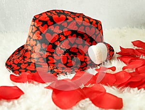 Valentines black hat with many red hearts, on white shag carpet, rose petals, small white pillow hat