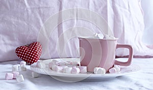 Valentines composition. Cup of hot chocolate with Marshmallows, on the bed. Small red heart on background.Breakfast