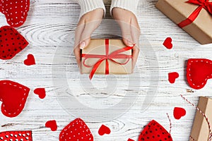 Valentines Day background. Female hands holding Valentines day gift above wooden table with red hearts. Top view. Xmas gift wrappi