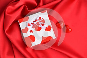 Valentines Day background. Hearts with gift box on red satin fabric background