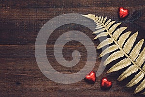 Valentines Day background, mockup with red heart shape chocolate candies and golden leaves on wooden background. Valentine Day,