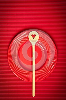 Valentines Day background with red plate and wooden spoon with heart on red background