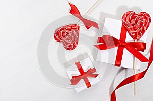 Valentines day background - white gift boxes with red silk bow, ribbon, lollipops hearts on white wood table, copy space.