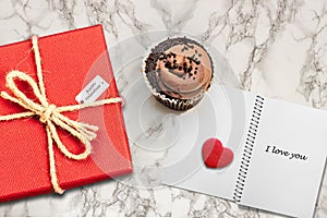 Valentines day card background with red present gift box on marble table next to chocolate cupcake love heart shape cookie and