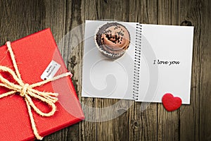 Valentines day card background with red present gift box on wooden table next to chocolate cupcake love heart shape cookie and