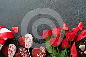 Valentines day card. Rose red flowers brownie cookies and chocolate candy on heart shaped, gift box with wine on black background.