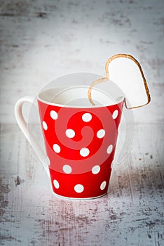 Valentines day concept. Coffee red polka dotted cup with a heart shaped homemade cookie over white wood background.