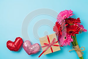 Valentines day concept with gerbera daisy flower bouquet, gift box and heart shapes  on blue background. Top view, flat lay