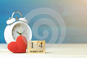 Valentines day concept. hand make yarn red heart beside wooden block calendar set on Valentines date 14 February in front of white