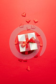 Valentines day concept. Red hearts, kraft surprise box with bow on a red background. Flat lay, top view, copy space Minimal