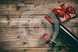 Valentines day. Red wine bottle, rose and a gift on wooden background