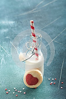 Valentines day cookies. Shortbread cookies inside sweet red heart on pink plate and bottle of milkshake on dark blue background. M