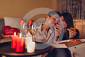 Valentines Day couple in love eating pizza drinking wine with strawberries having romantic dinner celebrating at home