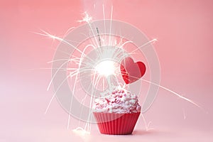 Valentines day cupcake. Cupcake with pink cream and sprinkled, with red heart and sparkler on a pink background. Concept postcard