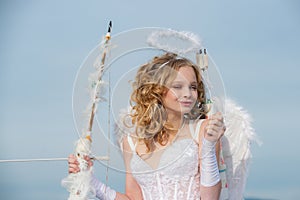 Valentines day cupid. Innocent Girl with angel wings standing with bow and arrow against blue sky and white clouds