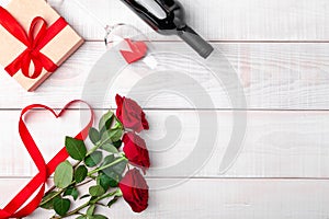 Valentines day dinner romantic setting, red tape, kraft gift box, heart in wine glass, bottle, roses, on white wooden