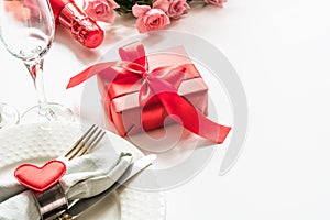 Valentines day dinner with table place setting with red gift, glass for champagne, a bottle of champagne, heart ornaments with sil