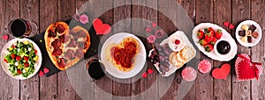 Valentines Day dinner table scene on a dark wood banner with heart shaped pizza, pasta, wine, cheese plate and desserts