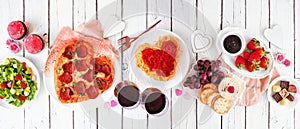 Valentines Day dinner table scene on a white wood banner with heart shaped pizza, pasta, wine, cheese plate and desserts