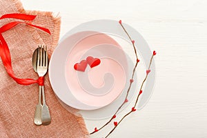 Valentines Day festive table setting on a white wooden table. Dinner meal in restaurant at Valentine Day. Two red hearts on pink