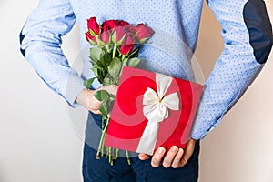 Valentines day gift surprise,man hiding gift and holding red rose bouquet