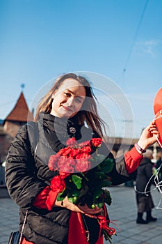 Valentines day gifts. Woman holding bouquet of red roses flowers and balloons on city street. Happy girlfriend