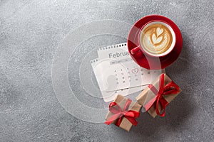 Valentines day greeting card. Red coffee cup and gift box over february calendar. Top view