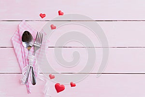 Valentines day and love concept. Fork and spoon with red hearts on pink pastel wooden background