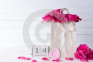 Valentines day and love concept. Pink roses in paper bag with February 14 text on wooden block calendar on white wooden background