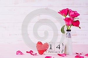 Valentines day and love concept. Pink roses in vase with February 14 text on wooden block calendar on white wooden background
