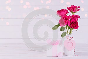 Valentines day and love concept. Pink roses in vase with wooden heart and gift box on white wooden background