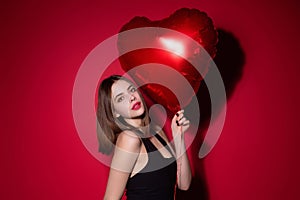 Valentines day, love heart. Portrait of lovely valentine girl hold red heart on red studio background. Beautiful woman