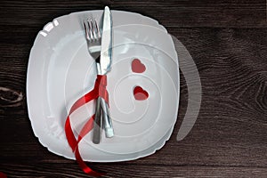 Valentines day meal background with red ribbon, hearts, fork, knife, white plate and napkin. Romantic holiday table