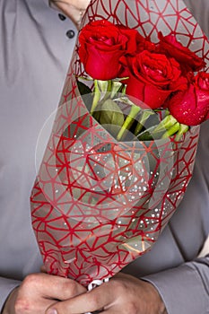 Valentines day or proposal. Young happy handsome man holding big bunch of red roses in his hand on grey background