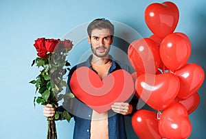 Valentines day romance. Young man with bouquet of red roses and heart balloons smiling, bring presents for lover on