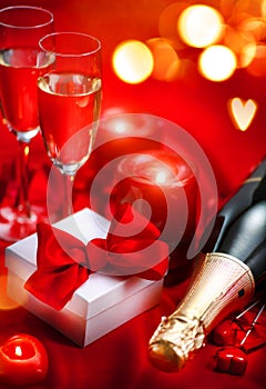 Valentines Day romantic dinner. Champagne, candles and gift box over holiday red background
