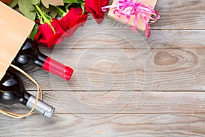 Valentines day romantic greeting card. Red rose flowers, wine bottles a shopping bag and gift box on wooden table. Free space