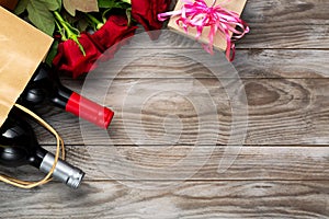 Valentines day romantic greeting card. Red rose flowers, wine bottles, shopping bag and gift box on wooden table. Free space