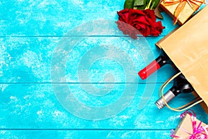 Valentines day romantic greeting card. Red rose flowers, wine bottles a shopping bag and gift boxes on blue wooden table. Free